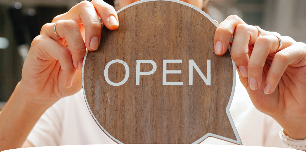 Wooden "OPEN" business sign in front of store owner. Close up shot. 